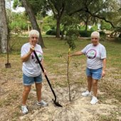Garden club members holding shovels near newly planted tree